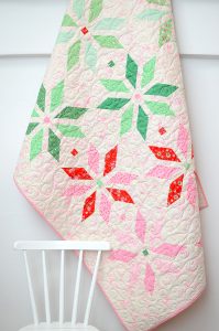 Christmas quilt hanging from a wall, a chair in the front